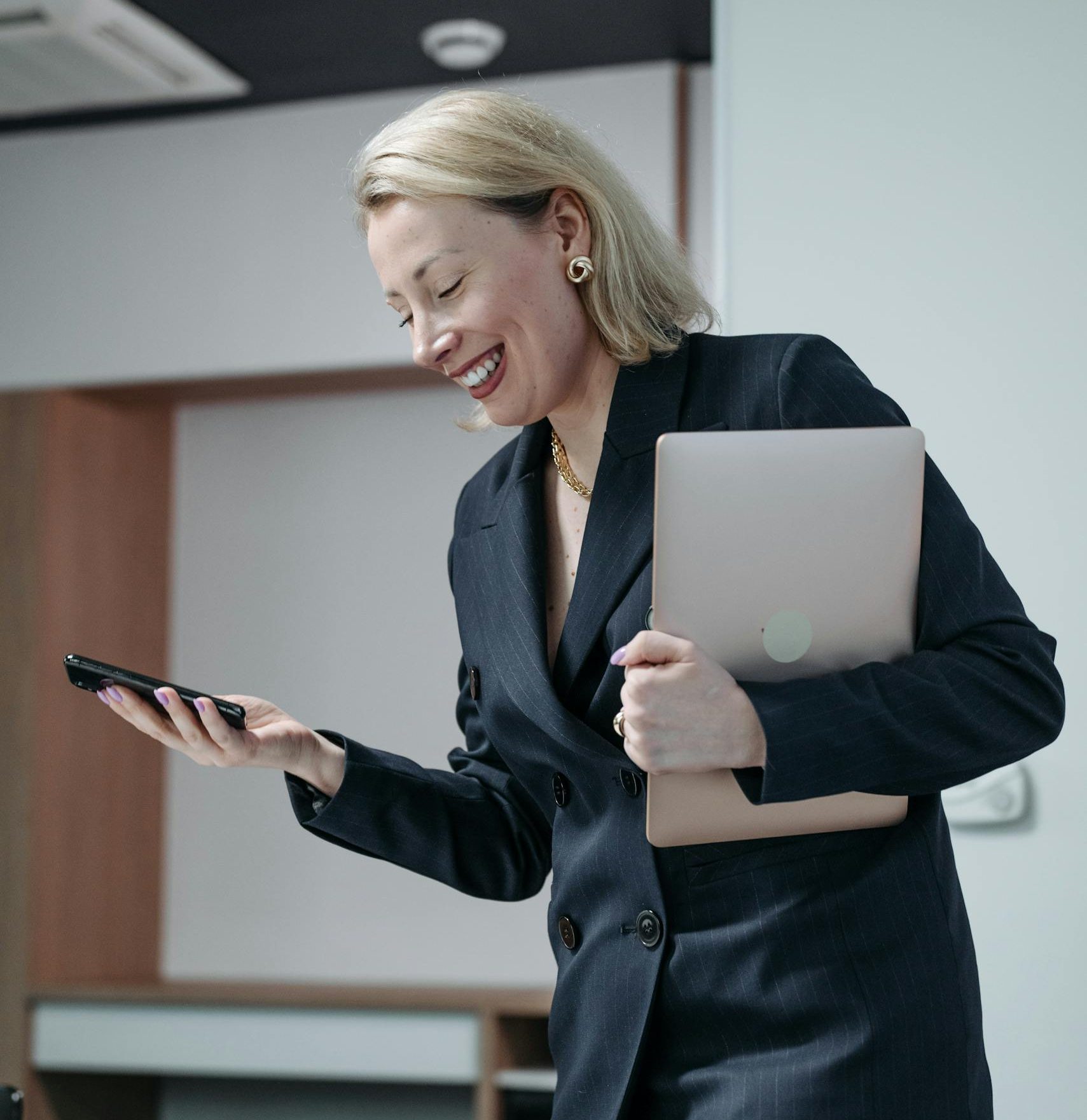 Smiling businesswoman multitasking with a laptop and smartphone in office.